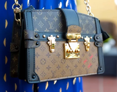 louis vuitton hand bag hanging from woman in blue and gold dress