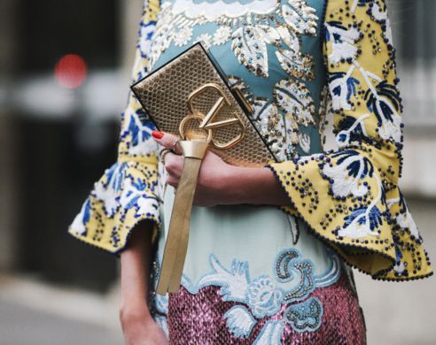 a woman holding a gold valentino clutch bag