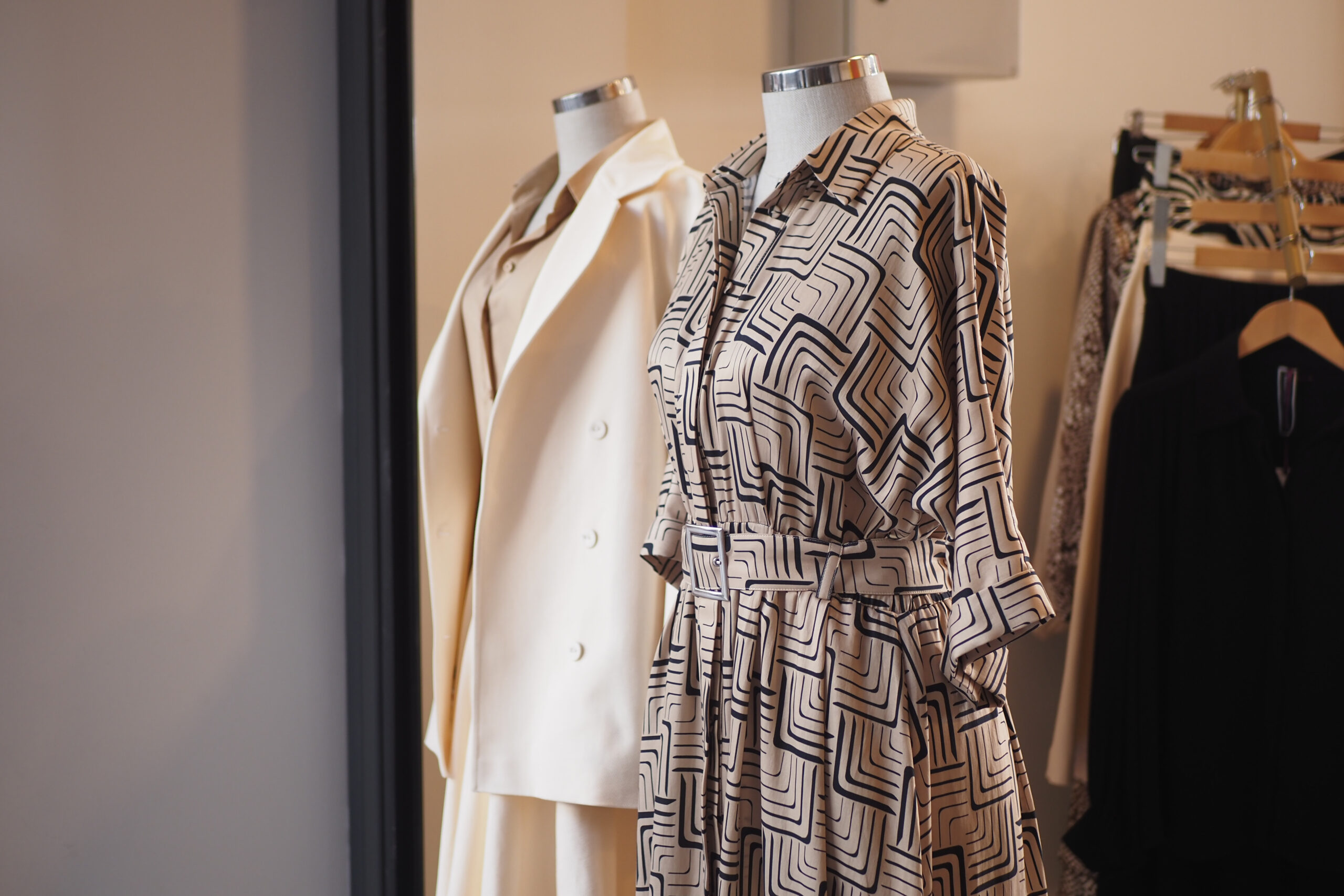 Mannequins showcasing a patterned beige dress and a cream blazer in a boutique setting.