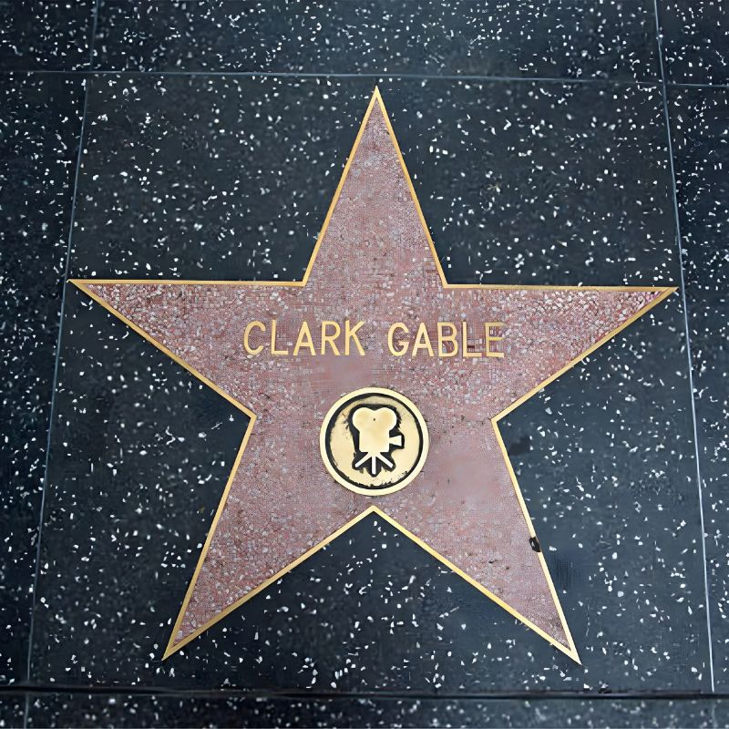 A Terrazzo And Brass Hollywood Walk Of Fame Star Honoring "clark Gable," Adorned With A Film Camera Symbol, Celebrates His Hollywood Heritage On The Black Speckled Sidewalk.