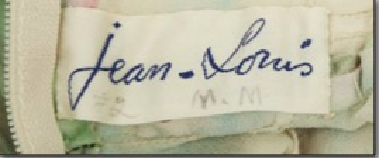 A Clothing Label With The Handwritten Name "jean Louis"—famed For Hollywood Heritage—features The Initials "m. M." Below In Smaller Letters, Suggesting A Jean Louis Designer Dress Possibly Linked To Marilyn Monroe.