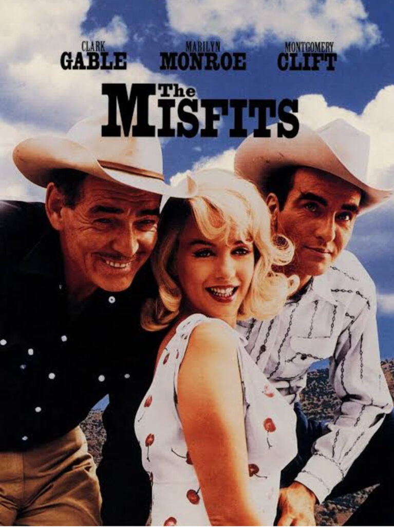 Film Poster For "the Misfits" Featuring Three People In Cowboy Attire Under A Blue Sky, With The Names Clark Gable, Marilyn Monroe—icon Of Hollywood Heritage—and Montgomery Clift Displayed Above The Title.
