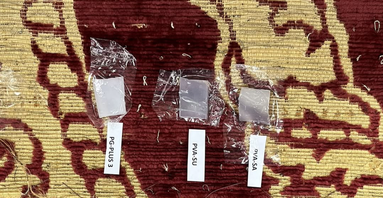 Three Labeled Plastic Samples—pg Plus 3, Pva Su, And Pva Sa—are Displayed On A Patterned Red And Yellow Surface, Each Wrapped In Transparent Plastic, Highlighting Innovations In Conservation For Cultural Heritage Preservation.