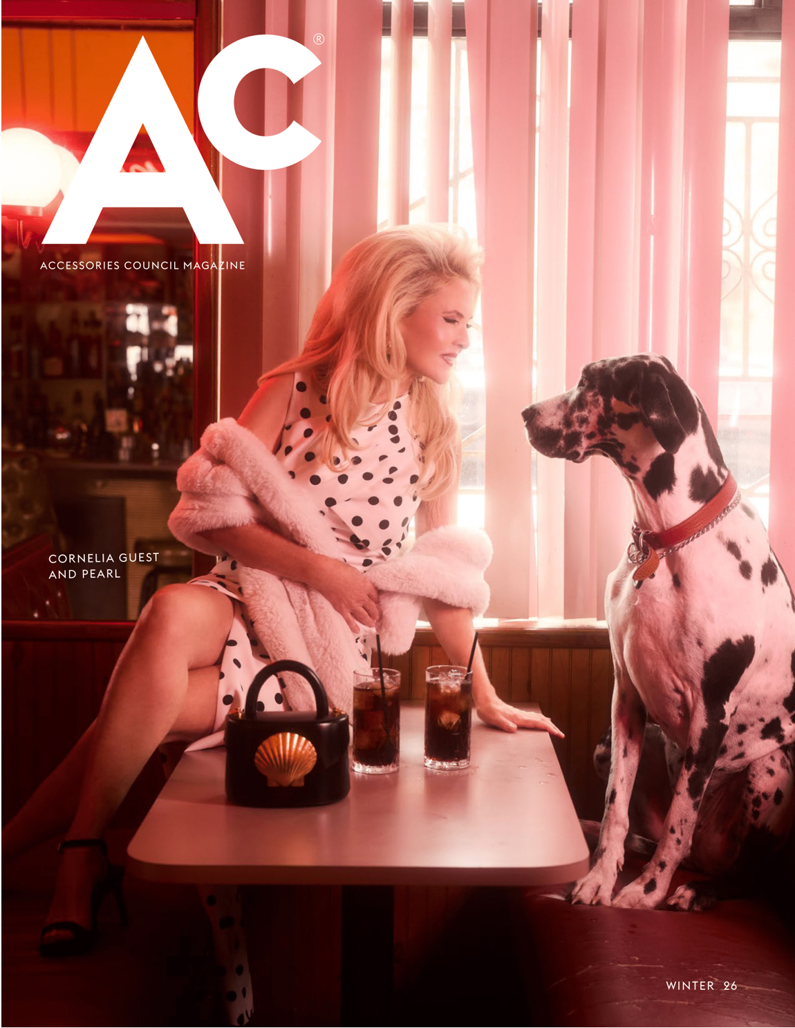 A Woman In A White Dress With Black Polka Dots Sits At A Diner Booth With A Large Dalmatian Dog; Two Drinks Are On The Table In This Chic Accessories Council Magazine Fifth Anniversary Issue Scene.