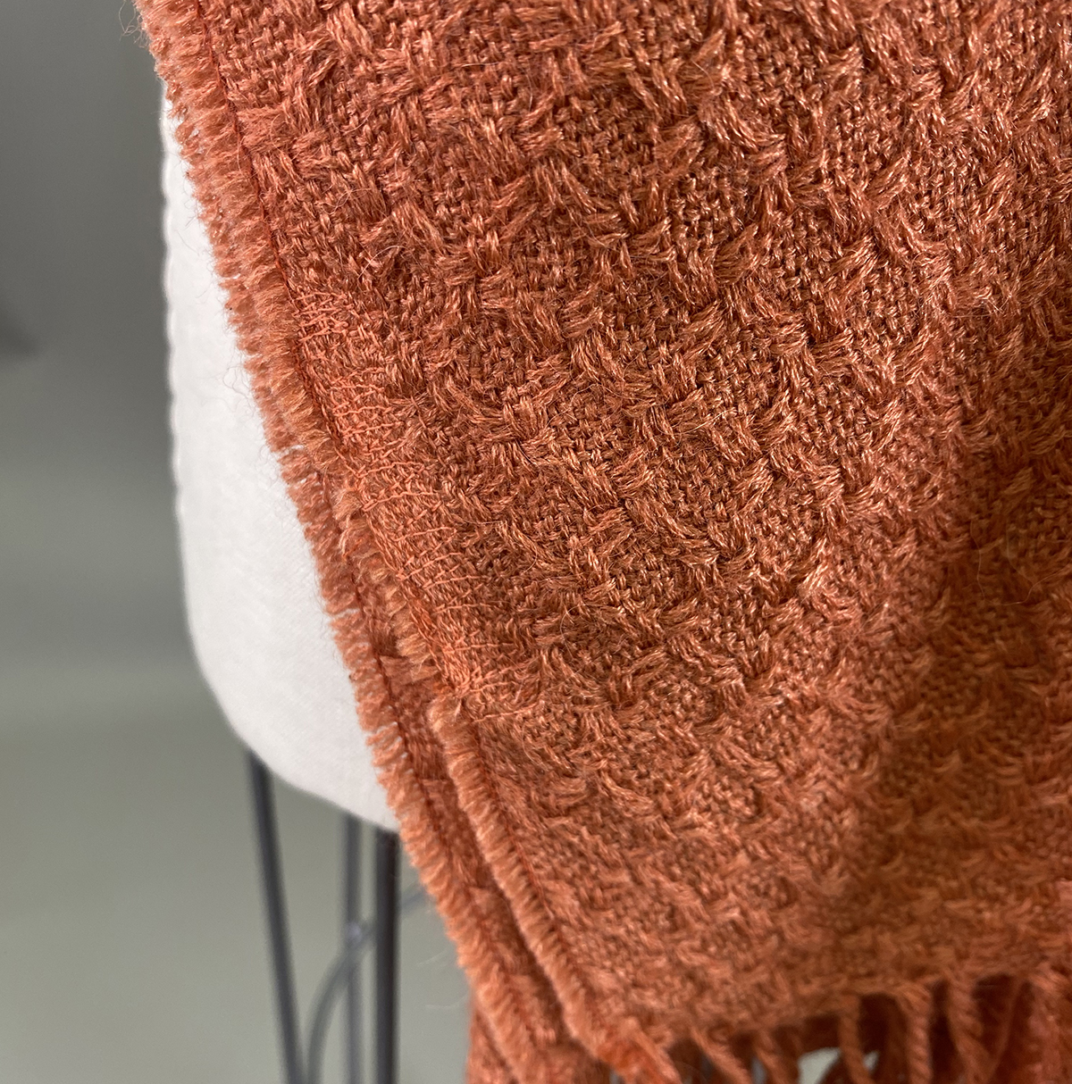 A Close Up Of An Orange Textured Woven Blanket Draped Over The Back Of A Light Colored Chair.