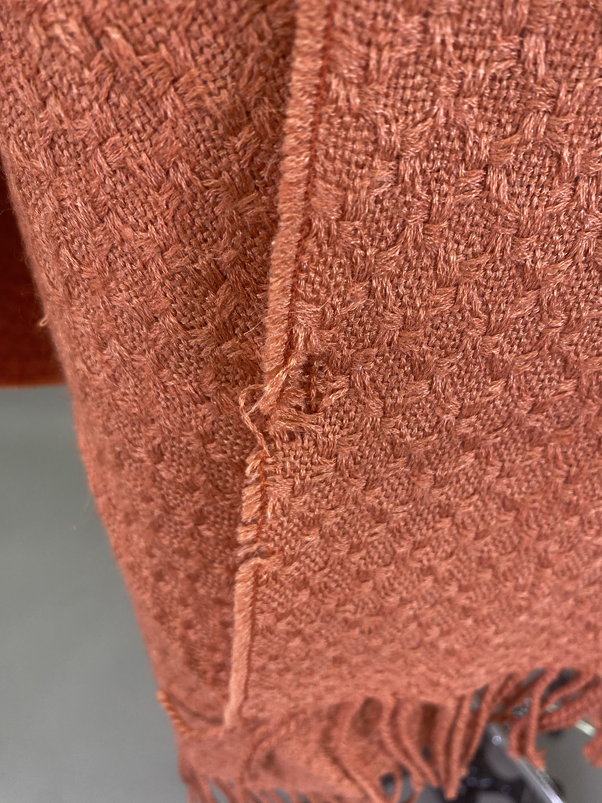 Close Up Of A Reddish Brown Woven Fabric With Visible Loose Threads And Slight Fraying Along The Edge.