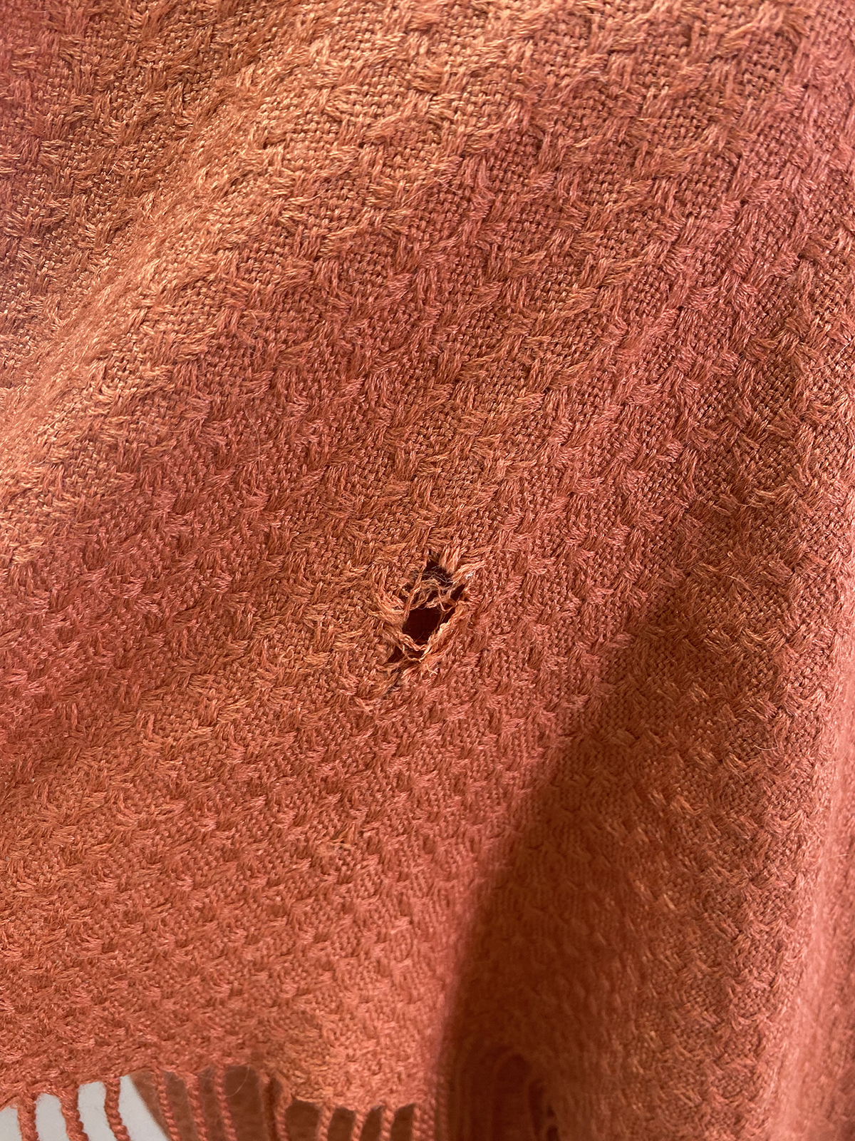 A Close Up Of An Orange Woven Fabric With A Small Hole In The Center And Fringed Edges At The Bottom.