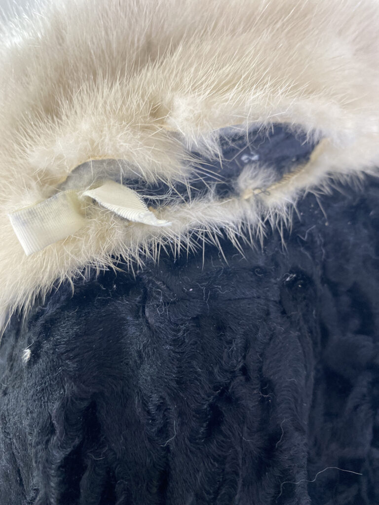 Close Up Of A Garment Made From Black Textured Fur With A Torn Seam, Revealing Beige Fur Trim And A White Fabric Ribbon Inside—a Detail Often Encountered During Professional Leather Cleaning Or Suede Care.