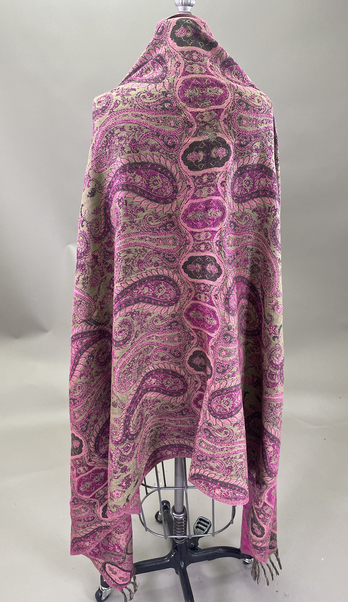 A Patterned Shawl With Pink, Purple, And Beige Paisley Designs Is Draped Over A Mannequin Against A Neutral Background.