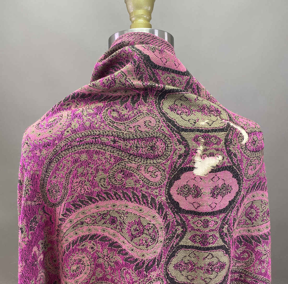A Mannequin Draped In A Pink Paisley Patterned Fabric With Green And Black Details; One Area Shows Visible White Thread Mending.